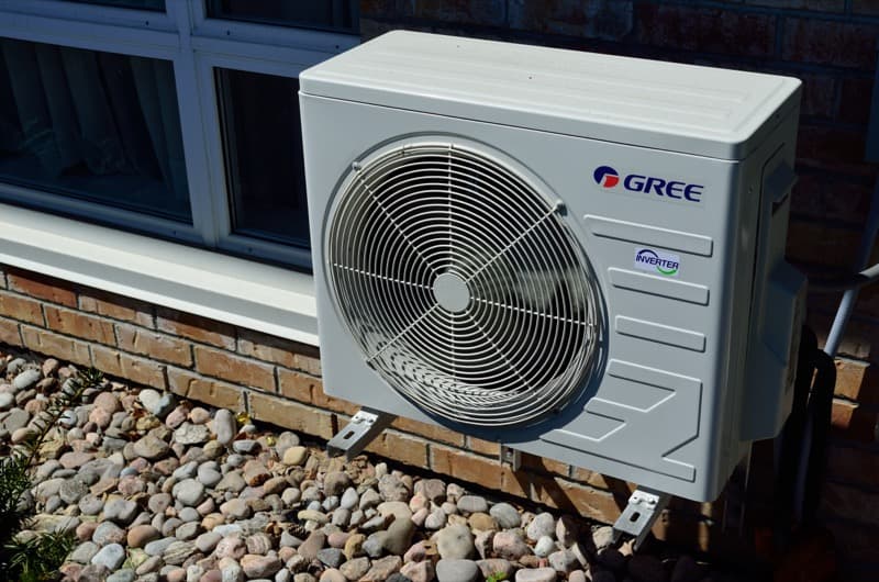 Unité extérieure de climatisation posée sur supports au pied d'une façade en briques